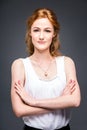 Portrait of a young redhaired beautiful girl in the studio on a gray isolated background. A woman is standing with her arms folded