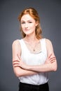 Portrait of a young redhaired beautiful girl in the studio on a gray isolated background. A woman is standing with her arms folded