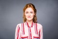 Portrait of a young red-haired beautiful girl in the studio on a gray isolated background. A woman stands and smiles in a red shir Royalty Free Stock Photo