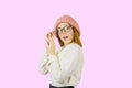 A portrait of a young red-haired girl in a knitted pink hat who is holding her glasses with her hand, opening her mouth Royalty Free Stock Photo