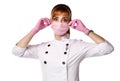 Portrait of young red-haired woman doctor or nurse in white medical uniform and gloves putting protective mask on face