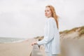 Portrait of young red haired woman in light blue sweater on sand beach by sea in storm Royalty Free Stock Photo