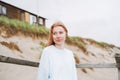 Portrait of young red haired woman in light blue sweater on sand beach by sea in storm Royalty Free Stock Photo