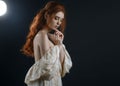 Portrait of a young red-haired woman in a vintage ash dress with open back and shoulders in the moonlight on a black background. A Royalty Free Stock Photo