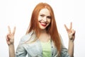 Portrait of young redhair woman looking at camera with smile and showing peace sign with fingers over white background