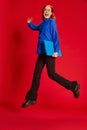 Portrait of young redhead girl in blue shirt and glasses posing in a jump with laptop over red background. Ambitions