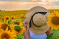 Portrait of young redhead girl hiding her face behind hat in sunflower field on sunset. Royalty Free Stock Photo