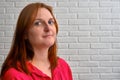 Portrait of a young redhead woman in red clothes on a background of a white brick wall Royalty Free Stock Photo