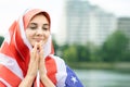 Portrait of young refugee woman with USA national flag on her head and shoulders. Positive muslim girl praying outdoors