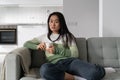 Young relaxed Asian woman looking at camera while sitting on sofa with cup of tea or coffee Royalty Free Stock Photo