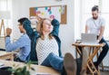 Portrait of young relaxed businesswoman with colleagues in a office, feet on desk.