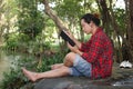 Portrait of young relaxed man in red shirt reading a book in beautiful nature background.