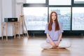 Portrait of young relaxed woman meditating sitting on floor in lotus position on background of window in bright office Royalty Free Stock Photo