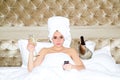 Portrait of young rich sensual beautiful woman watching tv drink champagne on bed. Sexy woman with towel on head Royalty Free Stock Photo