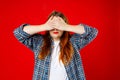 Portrait of young scared woman covering eyes with hands while standing against red studio background. Confused girl Royalty Free Stock Photo