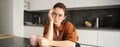 Portrait of young serious woman, working from home in glasses, sitting with folder and documents in kitchen, looking Royalty Free Stock Photo