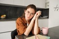 Portrait of young serious woman, working from home in glasses, sitting with folder and documents in kitchen, looking Royalty Free Stock Photo