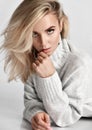 Portrait of young sexy flirting blonde woman vamp in warm knitted sweater looking at camera touching her lips Royalty Free Stock Photo