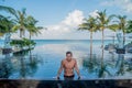 Portrait of young sexy handsome man model resting at the edge of the swimming pool at the tropical island luxury resort Royalty Free Stock Photo