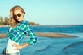 Portrait of young suntanned smiling blond wearing mirrored heart shaped sunglasses and checked blue shirt standing at the sea