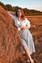 Portrait of young sexy woman on the haystack in morning sunlight, countryside. Beautiful woman in a dress sits on a Royalty Free Stock Photo