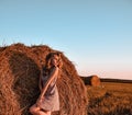 Portrait of young sexy woman with red hair on the haystack in morning sunlight, countryside. Beautiful woman in a dress sits on a Royalty Free Stock Photo