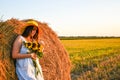 Portrait of young sexy woman with sunflowers on the haystack in morning sunlight, countryside. Beautiful woman in a dress sits on Royalty Free Stock Photo