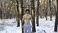 Portrait of young shirtless sportsman standing in snowy forest. Handsome strong athlete looking into camera after