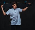 Portrait of a young skater boy dressed in a white t-shirt holds a longboard. on the dark background. Royalty Free Stock Photo