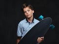 Portrait of a young skater boy dressed in a white t-shirt holds a longboard. Isolated on the dark background. Royalty Free Stock Photo