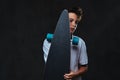 Portrait of a young skater boy dressed in a white t-shirt holds a longboard. Isolated on the dark background. Royalty Free Stock Photo