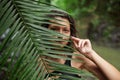 Portrait Young slender girl posing in the jungle hiding behind a palm leaf. Wildlife and a girl