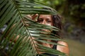 Portrait Young slender girl posing in the jungle hiding behind a palm leaf. Wildlife and a girl