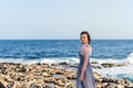 Portrait of a young slender graceful girl in a gray dress with pink feathers with a raging bright blue sea on the background Royalty Free Stock Photo