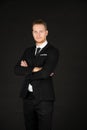 Portrait of young smart confident and successful businessman in black suit with arm crossed on isolated black background