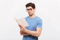 Portrait of young smart man in blue shirt wearing eyeglasses reading book with concentration, isolated over white background Royalty Free Stock Photo