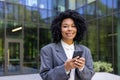 Portrait of a young smiling African American woman in a business suit standing outside an office building, holding a Royalty Free Stock Photo