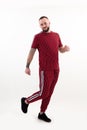 Portrait of young smiling bearded man with short dark hair wearing red striped sport wear, raising leg up, posing. Royalty Free Stock Photo