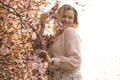 Portrait of young smiling beautiful woman with fair hair wearing pink cardigan, dress standing near bird-cherry tree. Royalty Free Stock Photo