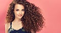 Portrait of young, smiling brown haired woman with voluminous and curly hairstyle.