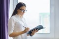 Portrait of young smiling businesswoman in the office, female in glasses holding documents near the window Royalty Free Stock Photo