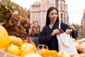 Portrait of young smiling casual woman happily looking for purse in bag at autumn farm shop