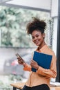 Portrait of a young, smiling, and cheerful African American businesswoman working in a casual office, holding a Royalty Free Stock Photo