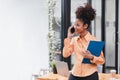 Portrait of a young, smiling, and cheerful African American businesswoman working in a casual office, holding a Royalty Free Stock Photo