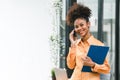 Portrait of a young, smiling, and cheerful African American businesswoman working in a casual office, holding a Royalty Free Stock Photo