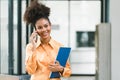 Portrait of a young, smiling, and cheerful African American businesswoman working in a casual office, holding a Royalty Free Stock Photo