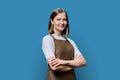 Portrait of young smiling confident woman in apron on blue background