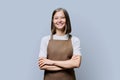 Portrait of young smiling confident woman in apron on grey background