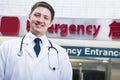 Portrait of young smiling doctor outside of the hospital, emergency room sign in the background Royalty Free Stock Photo
