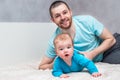 Portrait of a young smiling father with his infant in blue clothes on the bed in an embrace. Father`s day concept